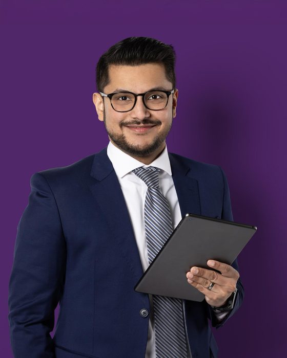 Un jeune homme à la peau mate et aux cheveux foncés, en tenue professionnelle, adopte une pose assurée avec une tablette à la main.