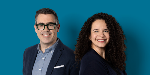 Deux personnes sourient à la caméra, soit un homme d’âge moyen à la peau claire, aux cheveux bruns grisonnants sur les côtés, qui porte des lunettes, et une femme à la peau mate et aux longs cheveux frisés foncés.