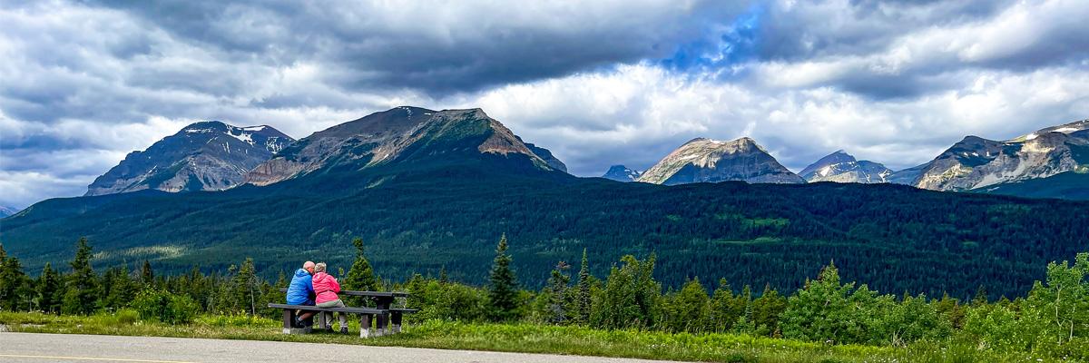 Certaines personnes âgées dépensent plus pour les loisirs. Un couple âgé assis sur un banc admire un paysage montagneux dans l’Ouest canadien.